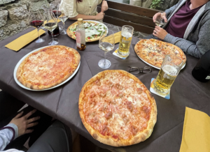 čtyři pizzy na stole, sklenice prosecca a vína, pivo